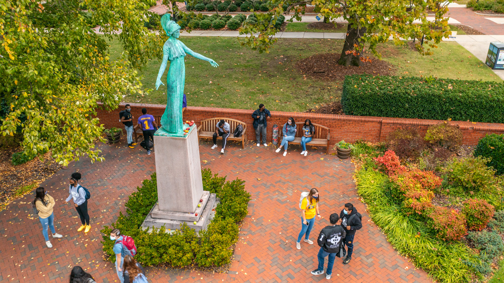 The Minerva statue in fall with students gathered below and walking by
